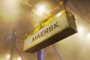 Industrial shipping container suspended by crane in Gdańsk port at night.